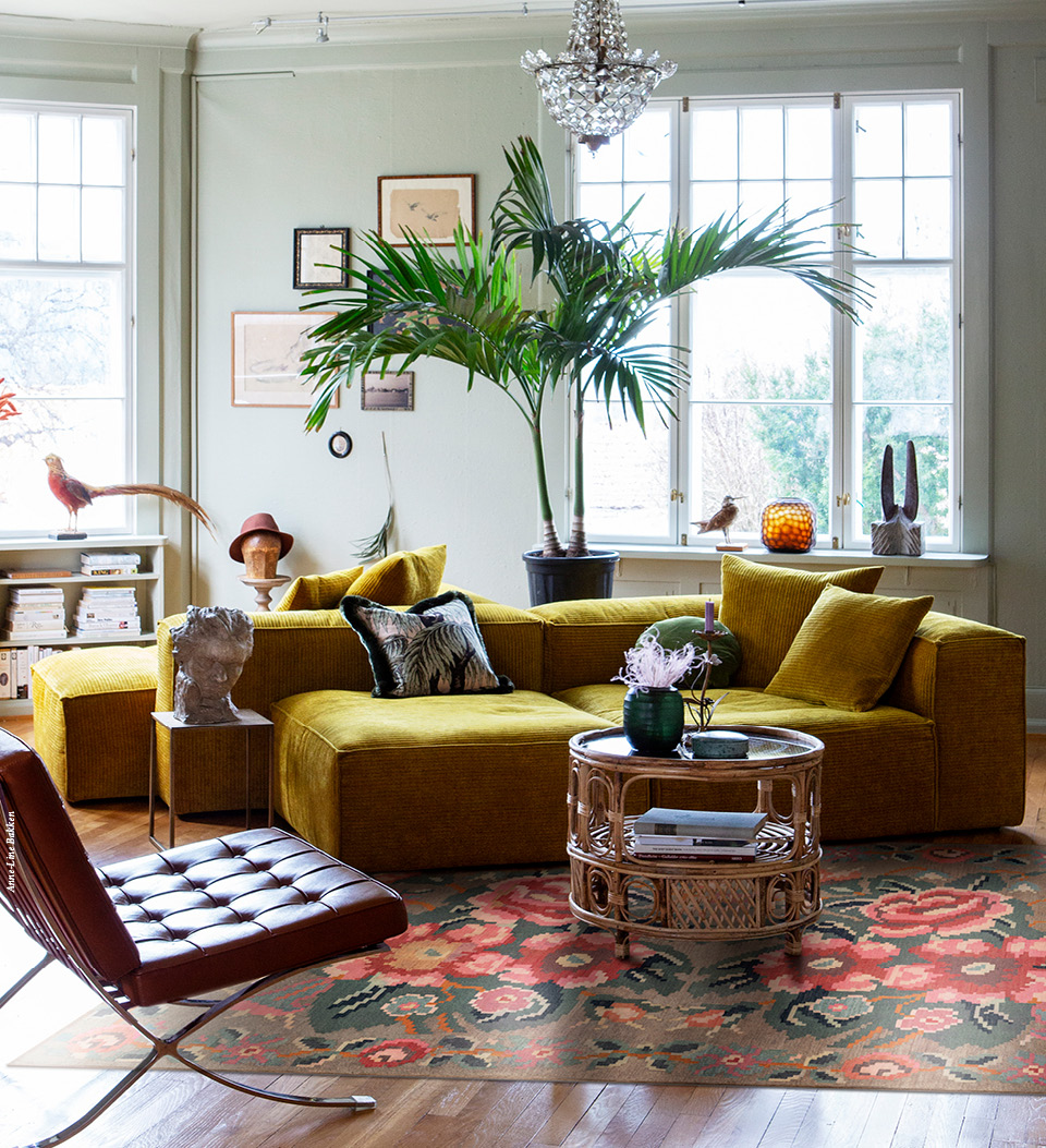 A living room with a yellowish sectional, a leather chair, and a floral rug