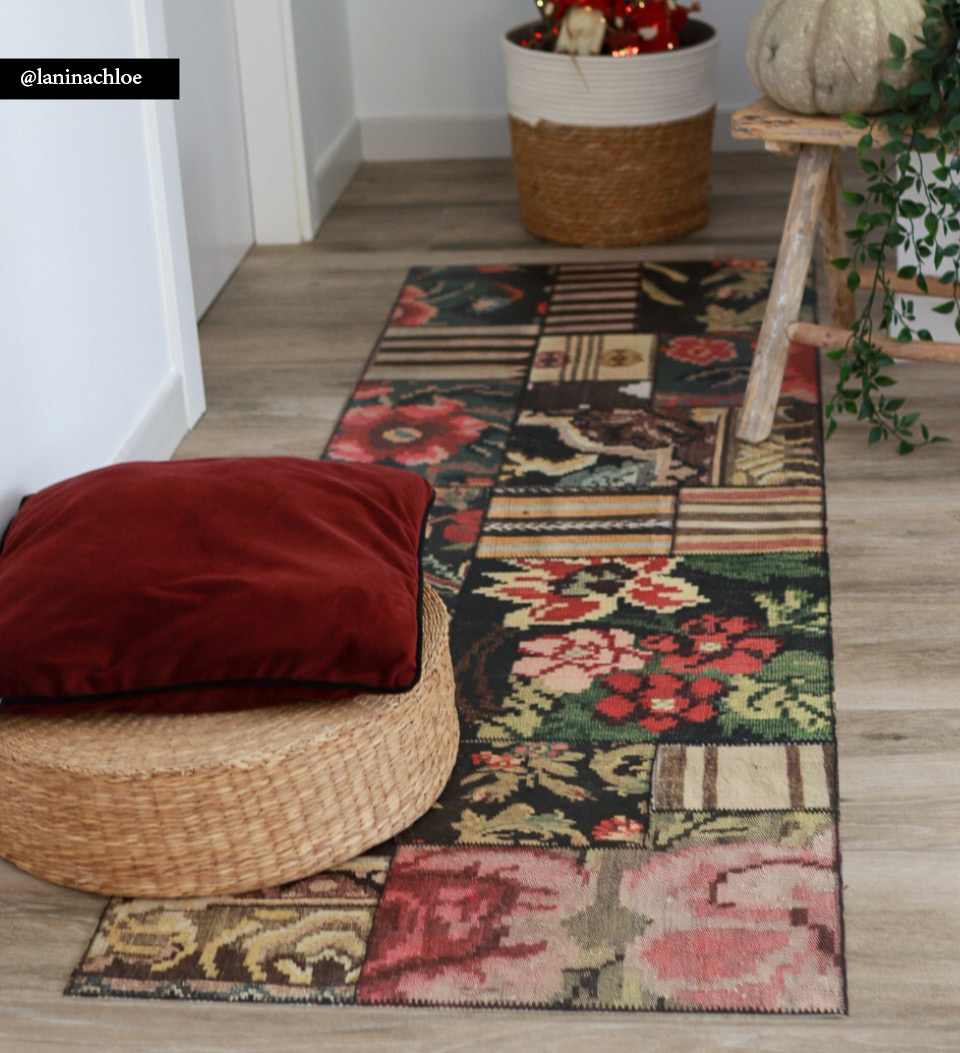 A colorful quilt kilim rug on a hallway floor with a wicker chair on top
