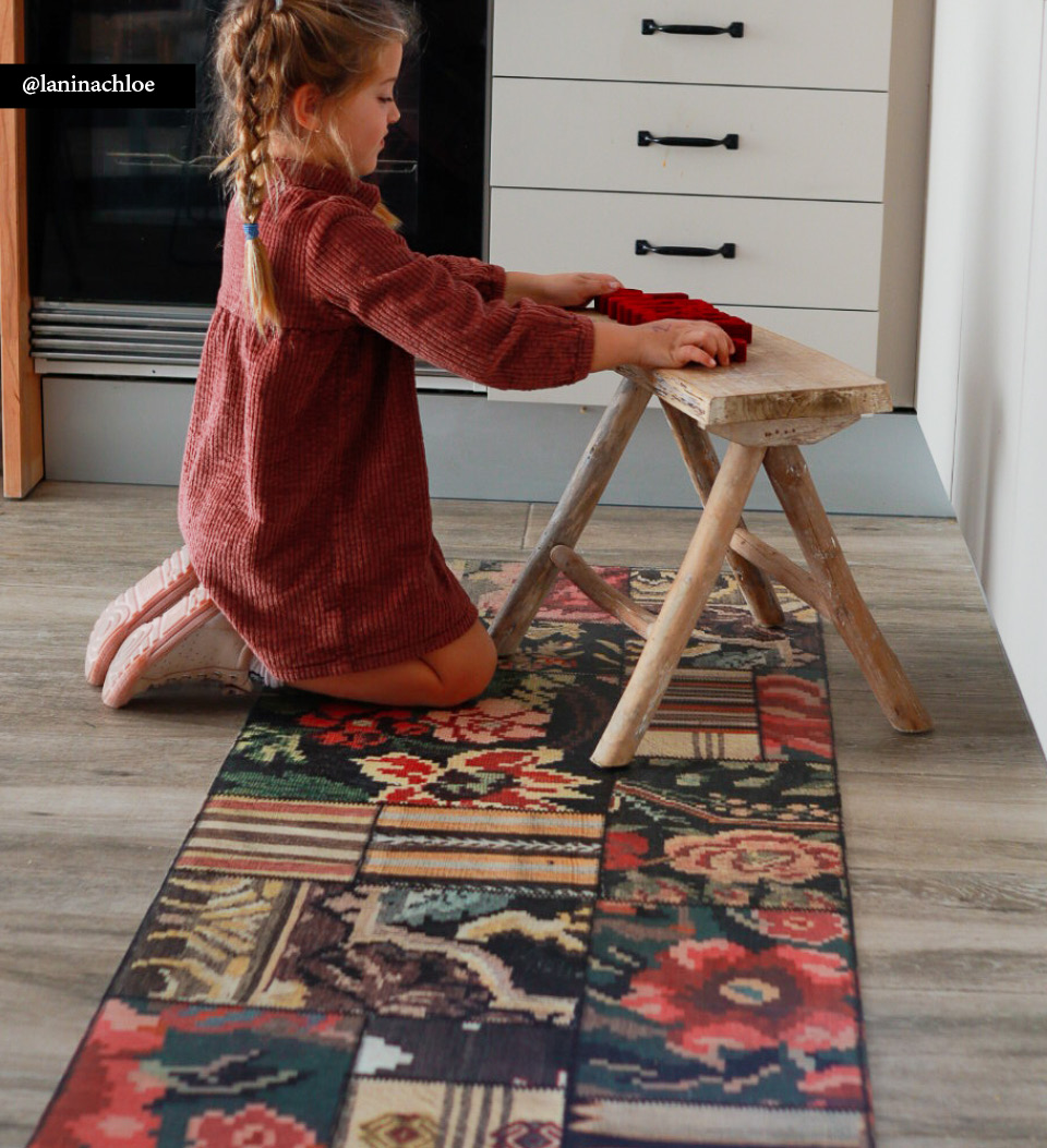 A young girl playing on a small wooden chair on top of a colorful kilim rug
