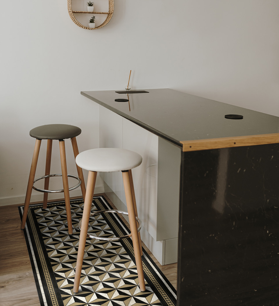 A geometric patterned  black and gold rug placed under bar stools