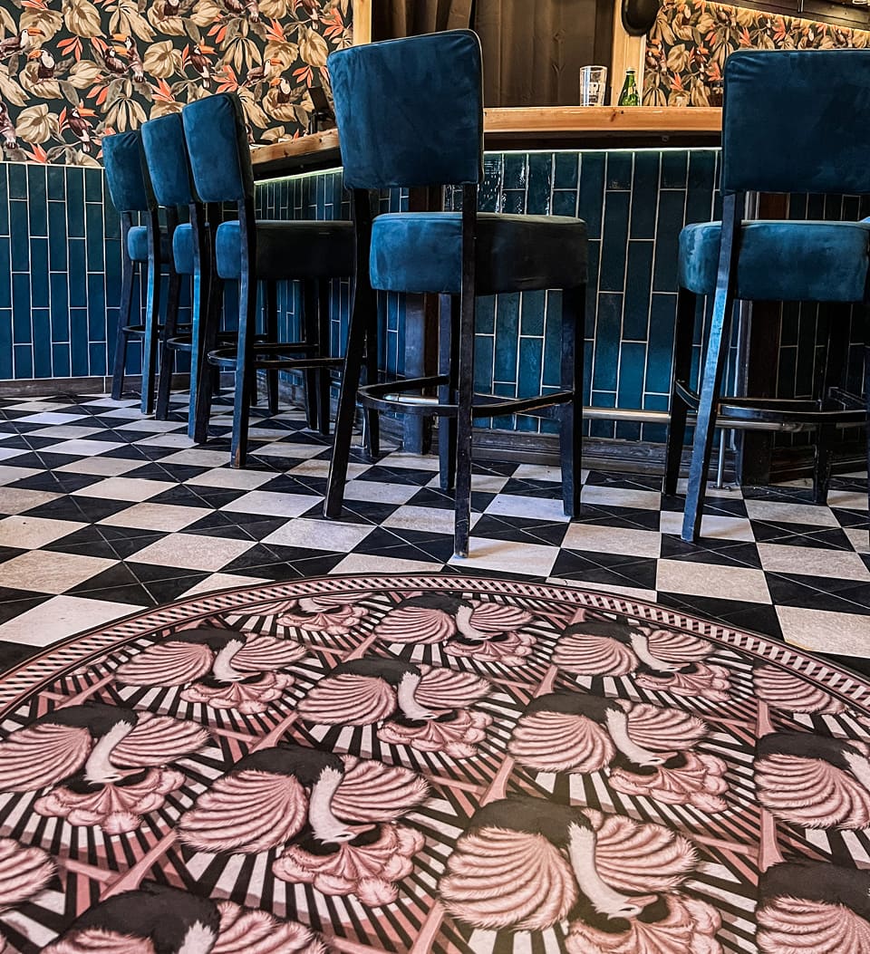 An ostrich-patterned round rug in pink hues on a black and white floor
