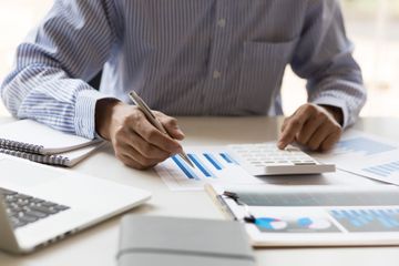 Businessman reviewing graphs on paper and open laptop with pen and calculator