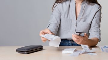 A businesswoman keeping track of expenses on her cellphone, through business receipts she has kept.