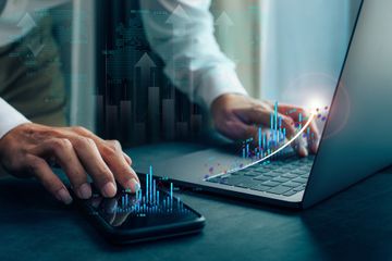 Man working on profit analysis with his cellphone and laptop on desk