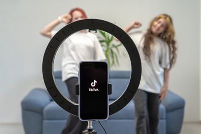 Two teens dancing in front of ring light and phone with TikTok display