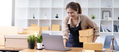 Woman holding boxes and using a laptop at a desk