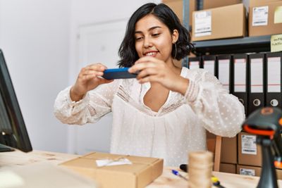 Woman taking picture of a box package in a office with other box packages