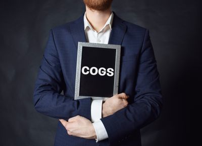 Man in a suit holding a sign reading COGS 