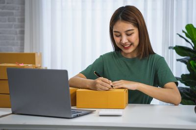 A young woman writing on a packaged product she is shipping to a customer while smiling