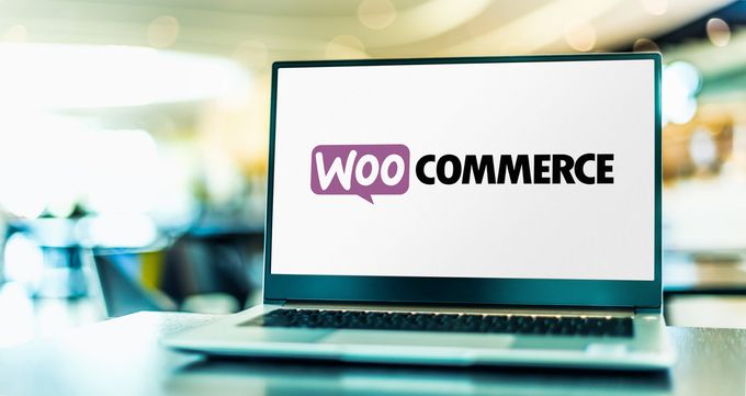 A laptop on a table showcasing the WooCommerce e-commerce platform logo on its screen