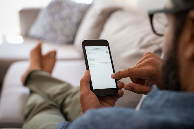 Man lying on couch while scrolling through messages on smartphone