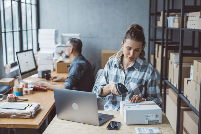 Woman scanning barcode on package with man in background looking at computer
