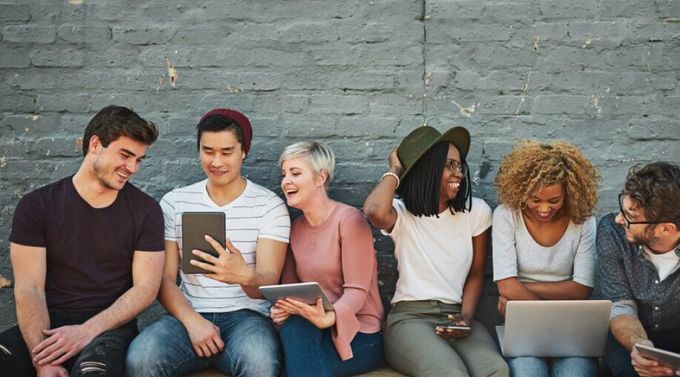 Group of young men and woman sitting outside on their phones and tablets