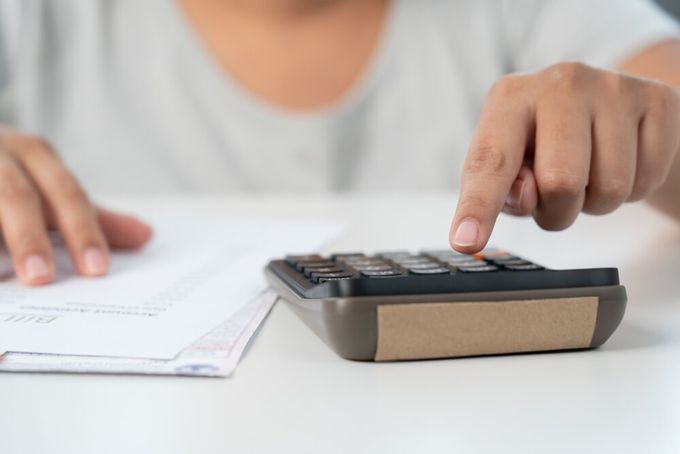 A person seated at their desk, busy punching numbers from a page in front of them into a calculator.