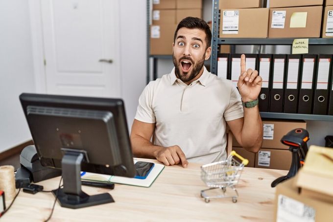 A young man seated at his office desk, with an expression seeming as if he has just had a great idea.
