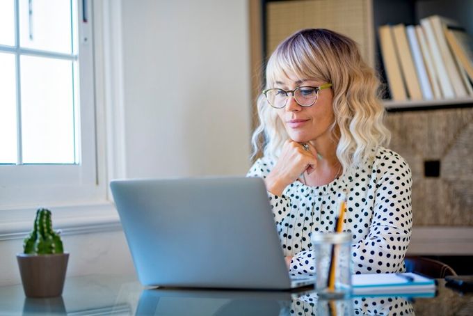 A young woman seated in her office, looking at her laptop screen, resting her chin on one hand.