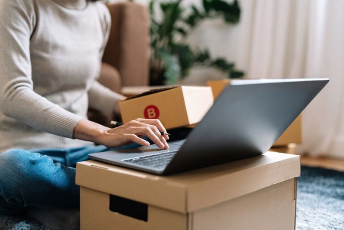 A dropshipper seated on their living room floor, working on their laptop, with various boxes visible.