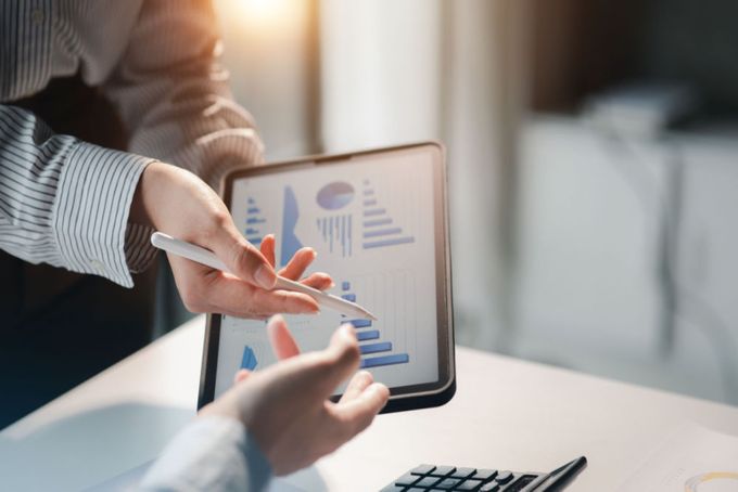 Two professionals both pointing towards a tablet, displaying a variety of bar charts and pie charts.