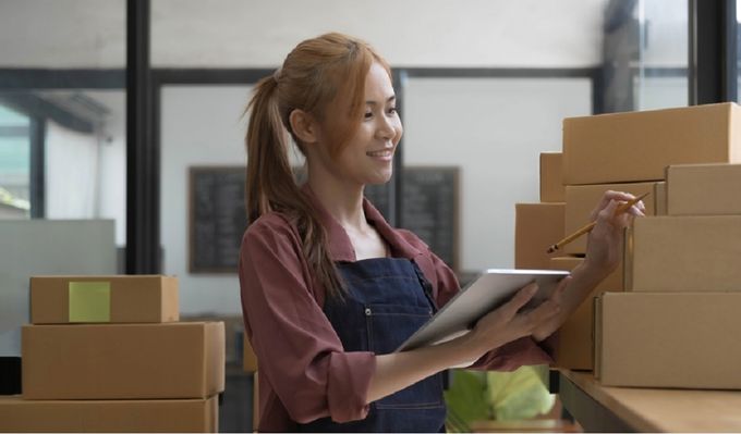 Woman holding a tablet and pen standing by boxes