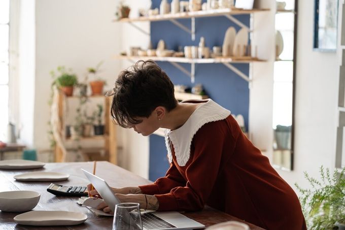 A female business owner hunch over at her office desk, performing calculations.