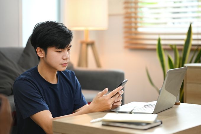 Person using phone and laptop at desk