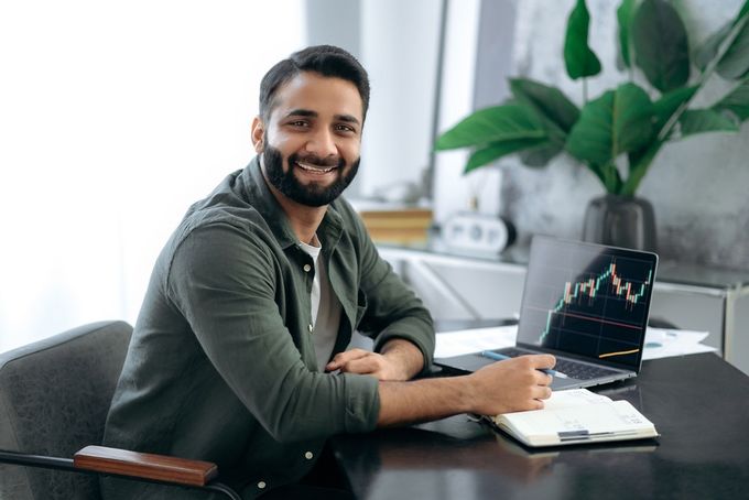 Smiling man holding a pen sitting by a desk