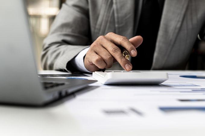 A man using a calculator by a laptop and documents