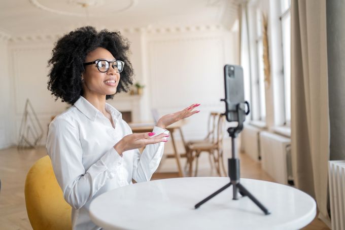 Woman with glasses sitting at table recording a video through mobile phone