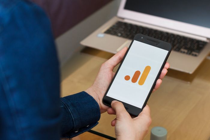 A professional seated at their desk with their phone in their hands, with the Google Analytics logo displayed on the screen.