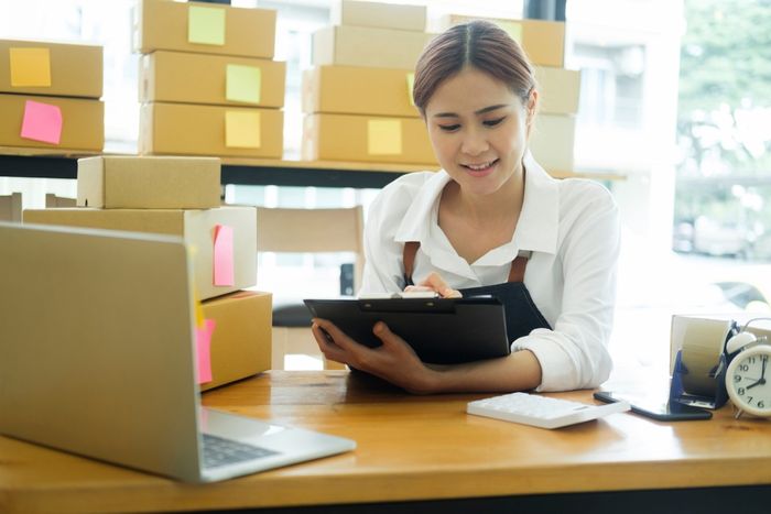 Young professional woman sitting at adesk while ticking items off on a clipboard