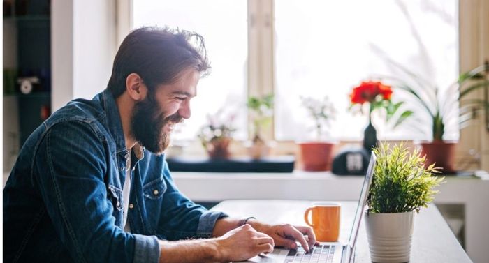 Man smiling while looking down at laptop next to coffee cup
