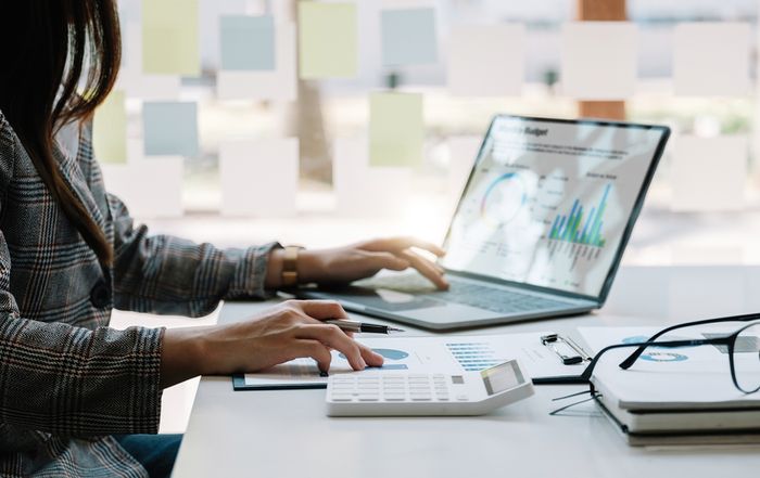 Businesswoman analyzing graphs on laptop and clipboard with calculator