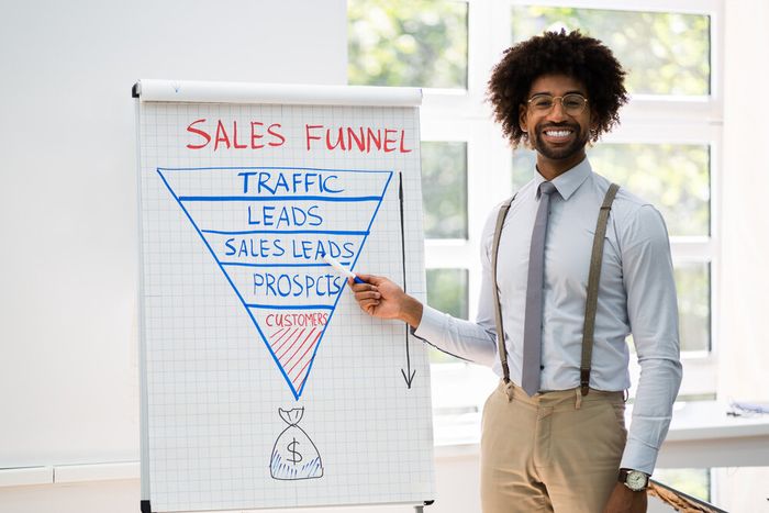 A professional smiling as he indicates towards something on a white board next to him.