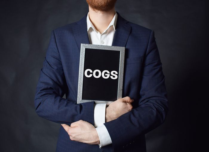 Man in a suit holding a sign reading COGS 