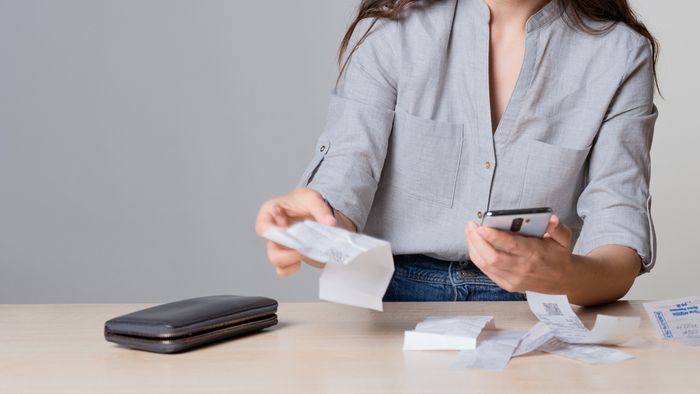 A businesswoman keeping track of expenses on her cellphone, through business receipts she has kept.