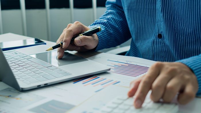 Man with revenue statistics on paper with pen in hand and a laptop to analyze revenue