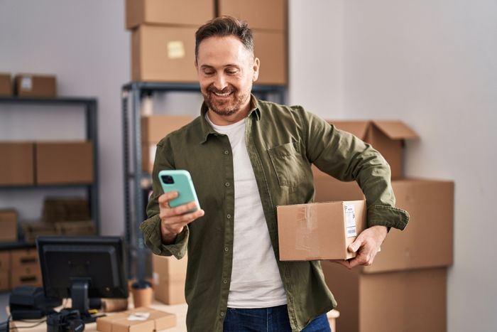 Happy man in a warehouse holding a phone and a shipping box