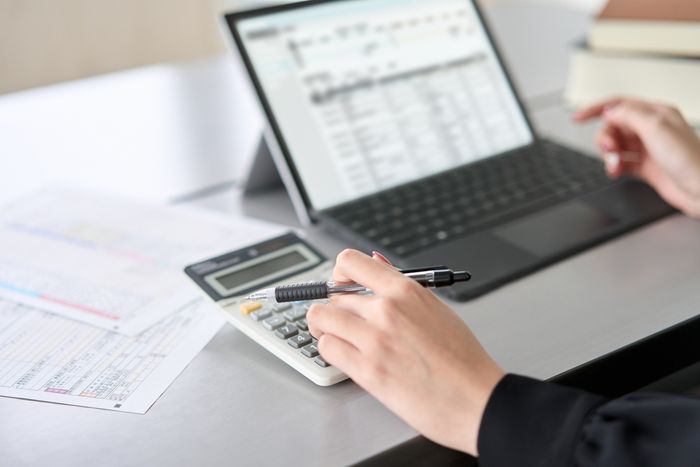 A person reviewing documents on a laptop while using a calculator