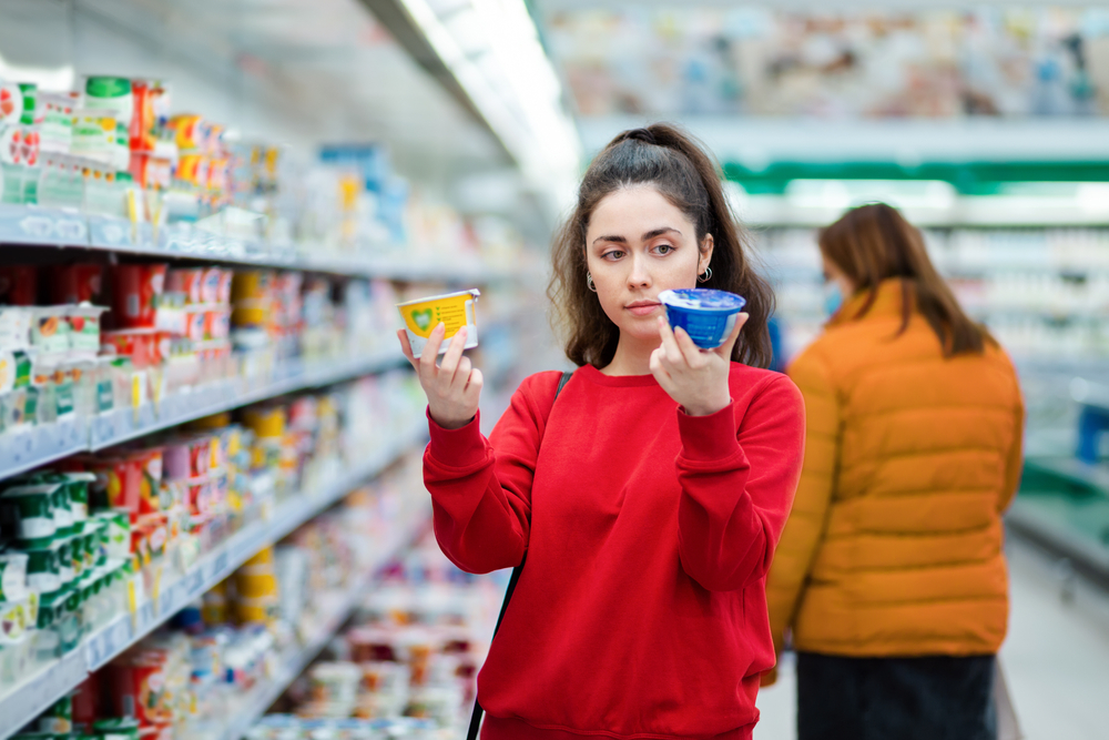 Woman in supermarket deciding between 2 different brands of the same product