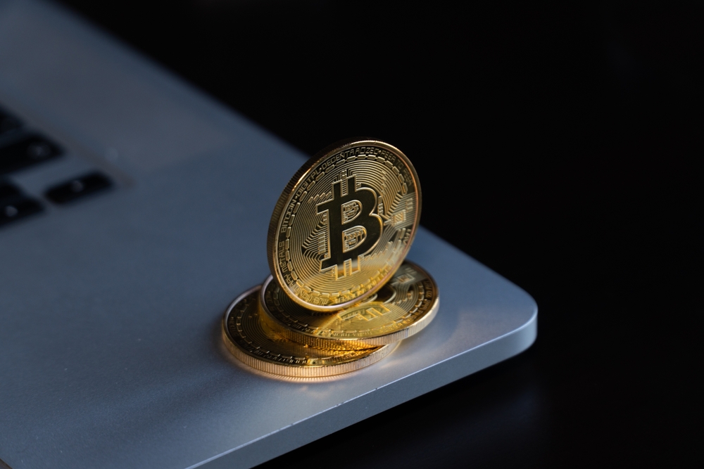 Three physical bitcoins balancing on the edge of a laptop