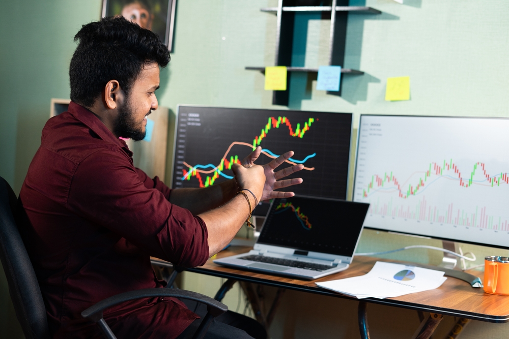 Man pointing to screens displaying stock prices rising and falling