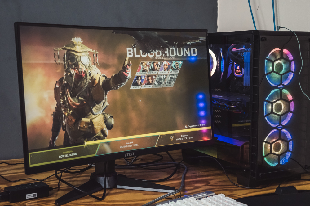 Gaming setup with RGB PC loading into an Apex Legends lobby and displaying Bloodhound on the screen