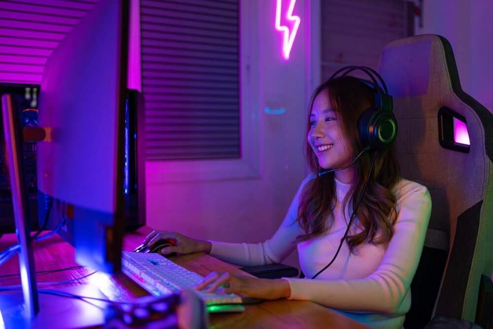 A happy PC gamer seated at her desk, with a headset on.