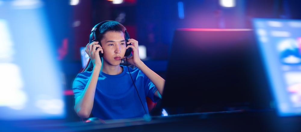 Young man looking focused while putting on his headset, and looking at his screen