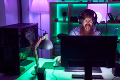 A gamer in a dimly lit room is yelling while playing a game on his PC