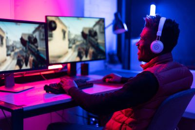 A gamer wearing a headset and playing a shooter game on two monitors