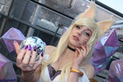 A girl cosplaying as an in-game character called Ahri, with fox ears, a crystal ball, with nine crystal tails behind her