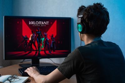 A gamer wearing headphones sitting in front of a computer preparing for Valorant Premiere