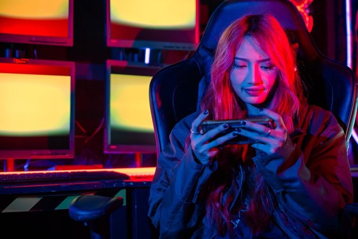 A girl seated in her gaming chair in a room lit with LEDs, busy with something on her phone.
