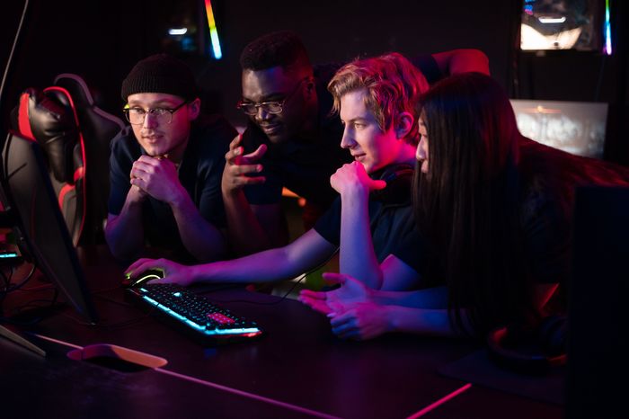 Group of gamers, three boys and a girl, in front of the computer, paying attention to what is on the screen
